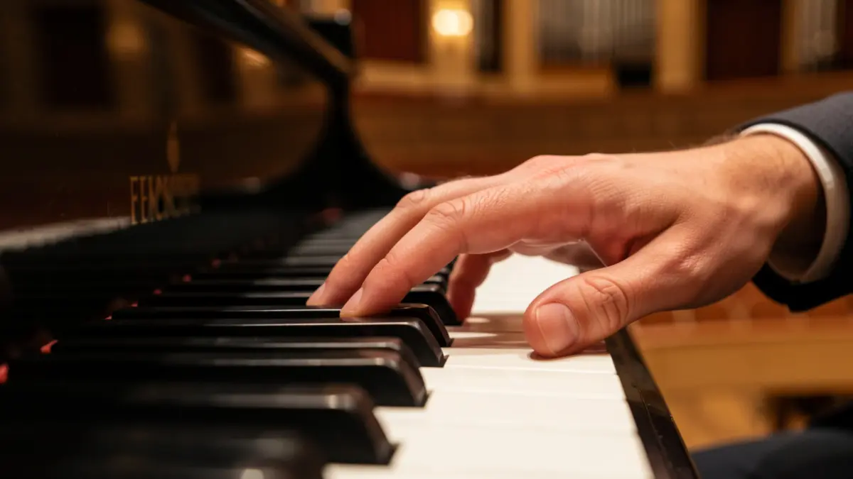 Gros plan sur des touches de piano avec une main qui en presse une, éclairage d'ambiance doux, faible profondeur de champ, évoquant l'improvisation et la création musicale.