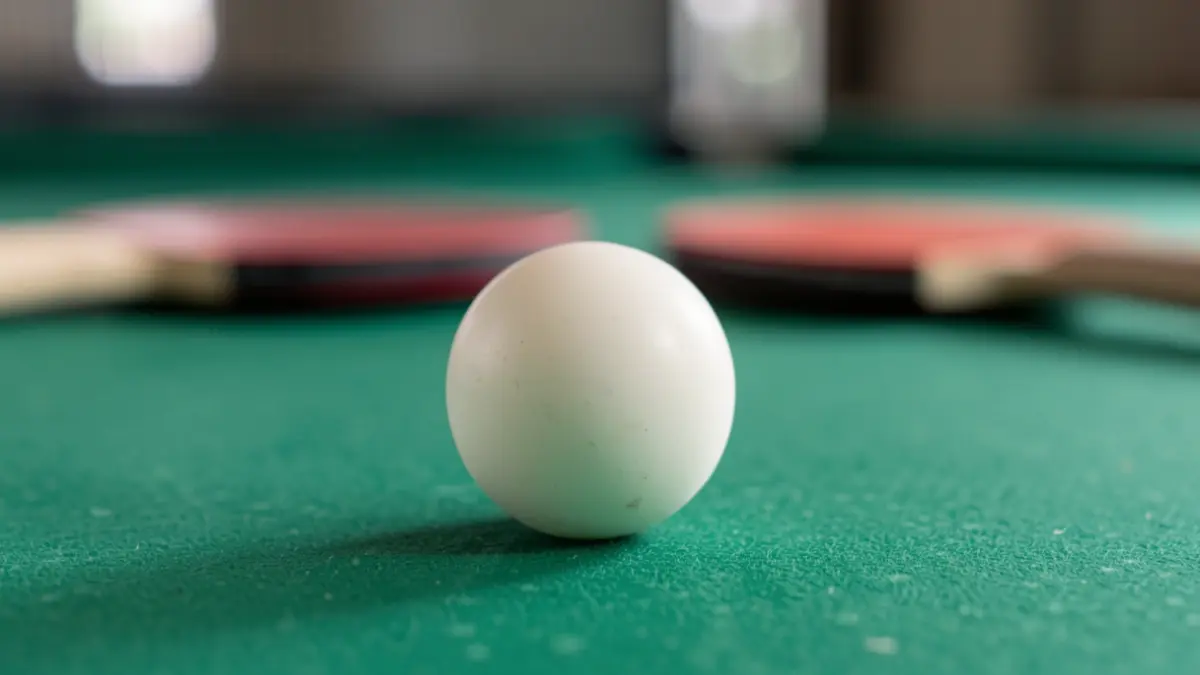 Generic image of a table tennis ball on a green table, with blurred paddles in the background.